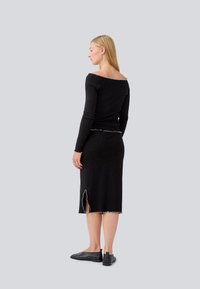 Haut long à manches noires avec un décolleté dénudé des épaules ; associé à une jupe noire assortie avec une fente sur le côté et des accents de couture blanche.