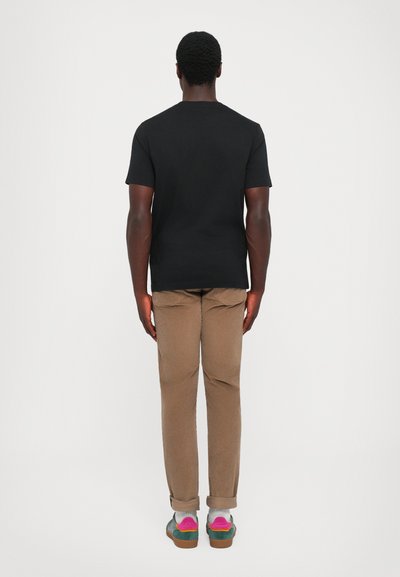 Black short-sleeve t-shirt, brown rolled-up pants, colorful shoes with pink and green accents, viewed from the back against a white background.