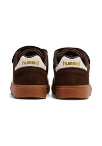 Brązowe zamszowe sneakersy z białymi akcentami, wyposażone w gumową podeszwę, złote logo i wyściełany kołnierz. Model bez sznurowadeł, łatwy do założenia.