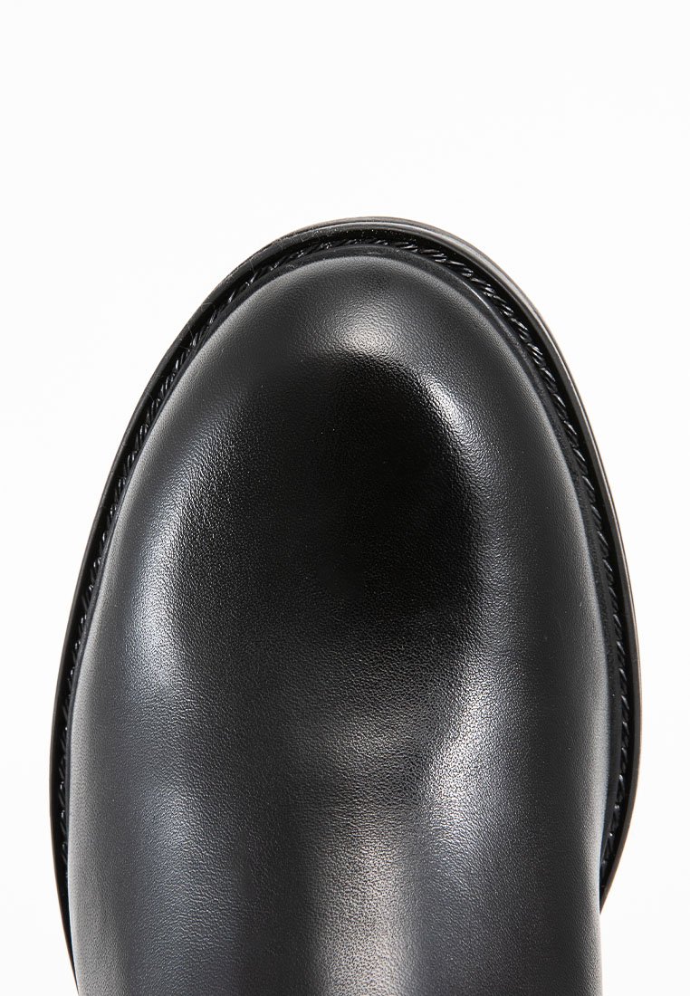 Schwarzer Lederschuh mit runder Zehenform, glatter Textur, dekorativer Naht entlang der Kante und glänzender Oberfläche.
