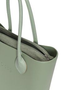 Grön tote-väska i mjukt material med två långa handtag. Har en dragkedjeficka och en kontrasterande strukturfoder.