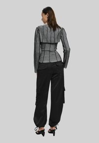 Tætsiddende, struktureret grå og sort jakke med bred bagpanel; parret med løse sorte cargo bukser med sidelommer og dekorativ syning.