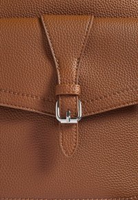 Borsa in pelle marrone con texture, dotata di un pattina e di una tracolla triangolare infilata in una fibbia metallica rettangolare argentata.