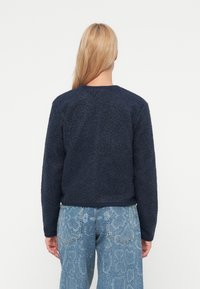 Marineblå fleecegenser med teksturert mønster, rund hals og lange ermer, kombinert med lyseblå slangeprint vide bukser.