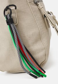 Beige Taschenhandtasche mit Struktur und Reißverschluss, mit bunten, geflochtenen Trägern in Grün, Rot, Schwarz und Weiß, die an einem Metallring befestigt sind.