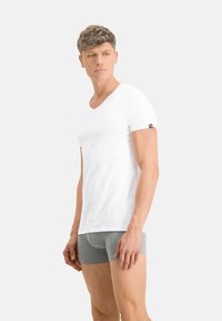 Weißes V-Ausschnitt-T-Shirt aus weichem Baumwollmaterial, körpernaher Schnitt mit kurzen Ärmeln, kombiniert mit grauen Boxershorts. Minimalistischer Stil und klare Linien.
