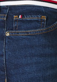 Jeans de mezclilla azul oscuro con costuras amarillas de contraste, una pequeña etiqueta roja, blanca y azul, y un diseño clásico de bolsillo trasero.