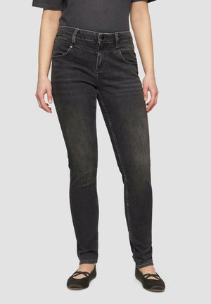 Schwarze Slim-Fit-Jeans mit einer gefleckten Textur, Fünf-Taschen-Design, Reißverschluss und Knopfverschluss, kombiniert mit schwarzen flachen Schuhen.