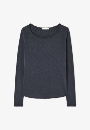 Tamsiai mėlynas ilgomis rankovėmis marškinėliai su plačiu iškirpimu, tekstūruota medžiaga ir laisva siluetu. Pasižymi raglan formos rankovėmis ir šiek tiek kreivu apdailos kraštu.