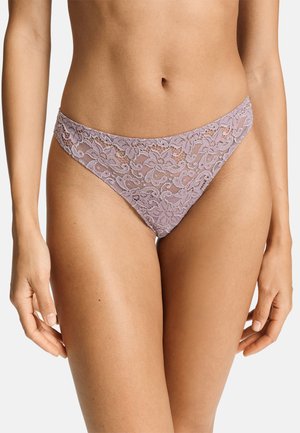 Mujer con ropa interior estilo bikini de encaje floral de color púrpura claro, mostrada desde la cintura hasta la parte superior de los muslos sobre un fondo liso.