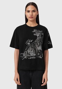 Μαύρο κοντομάνικο μπλουζάκι με μεγάλο αστραφτερό ασημί σχέδιο τίγρης. Το ύφασμα φαίνεται λείο με άνετη γραμμή και στρογγυλή λαιμόκοψη.