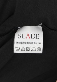 Sort tag i sort stof med "SLADE" i røde bogstaver. Materiale: 100% bomuld. Plejesymbolet inkluderer vaske-, tørre- og strygeanvisninger.