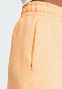 Calções leves de cor pêssego com uma textura suave, apresentando um cós elástico e um detalhe de bolso lateral.