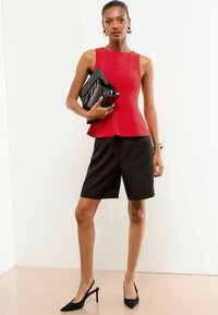 Rode mouwloze peplum top, zwarte op maat gemaakte shorts, zwarte leren clutch en zwarte slingback hakken. Soepele texturen met strakke lijnen.