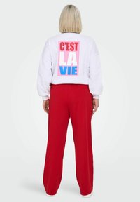 Siv svetri z oversize krojem z grafikami "C'EST LA VIE" v roza, rdeči in modri barvi, v kombinaciji z ohlapnimi rdečimi hlačami. Mehka tkanina, sproščen kroj.