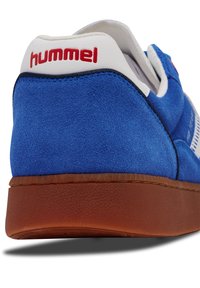 Baskets en velours bleu avec des accents blancs et rouges, dotées d'une semelle en caoutchouc marron et d'un dessus texturé distinct pour une meilleure adhérence et un confort optimal.