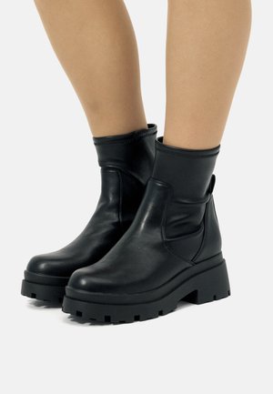 Botines negros de cuero suave con una suela gruesa y estriada y un caño ajustado. Incluyen una lengüeta lateral para facilitar su uso.