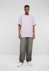 Lyselilla oversized t-skjorte med korte ermer, parret med løstsittende falmede jeans og hvite sneakers. Enkel logo detalj på brystet.