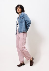 Lichtblauwe spijkerjas met een borstzak, gecombineerd met roze, high-waisted broeken. Bruine instappers maken de outfit compleet.