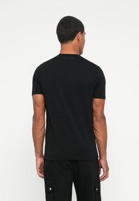 Camiseta de algodón negra con mangas cortas, cuello redondo y un logotipo discreto en la parte posterior cerca del escote. Textura suave.