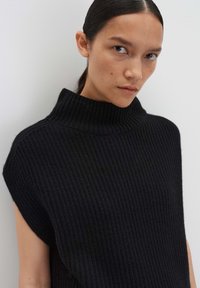 Pull en maille noir avec un col roulé haut, présentant une texture côtelée et de larges ouvertures pour les bras. Le tissu semble doux et épais.