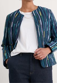 Kurtka pikowana w pionowe niebieskie i zielone paski, z okrągłym dekoltem, długimi rękawami oraz otwartym przodem, noszona na białej koszuli.