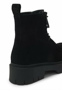 Bottine en daim noir avec semelle épaisse texturée, fermeture à lacets à l'avant et languette de tirage à logo à l'arrière.