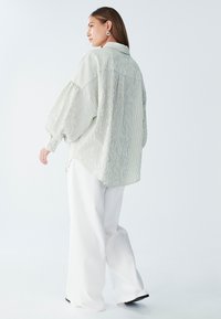 Svietlozelená pruhovaná oversize košeľa s balónovými rukávmi, gombíkovým golierom a zakriveným lemom, skombinovaná s bielymi širokými nohavicami.