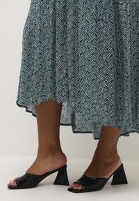 Czarne sandały na obcasie z wzorem krokodyla, kwadratowy czubek, noszone z niebieską spódnicą w wzór paisley z zielonymi i białymi akcentami.