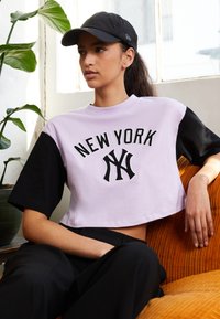 T-shirt cropped con maniche corte, blocchi di colore lavanda e nero, con la scritta "NEW YORK" e il logo NY ricamato in nero.