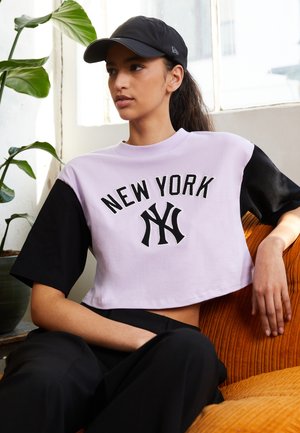 Kurzärmliges, verkürztes T-Shirt mit lila und schwarzen Farbblöcken, versehen mit "NEW YORK" und dem NY-Logo in schwarzem Stick.