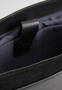 Interno di una borsa in pelle nera con una superficie liscia; presenta un rivestimento in tessuto scuro e un anello in pelle nera. Nessun hardware visibile.