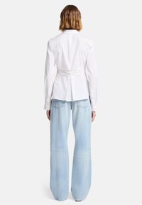 Vit figursydd skjorta med en skräddarsydd baksida, med långa ärmar och knutar vid midjan. I kombination med ljusblå vida jeans.