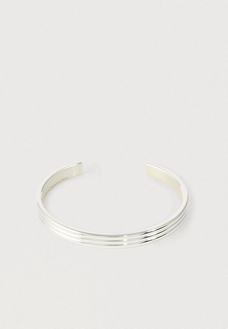 Srebrna bransoletka na mankiet z trzema równoległymi rowkami, w otwartym wzorze, umieszczona na białej powierzchni.