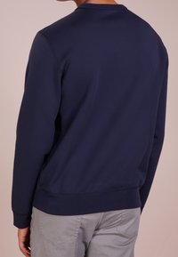 Mörkblå sweatshirt med rundhals, utrustad med ribbade ärmslut och nederkant, tillverkad av mjukt material. Sedd från baksidan, visar minimal design.