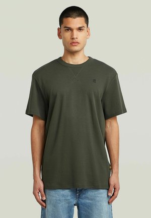 Camiseta de manga corta verde oliva hecha de algodón, con cuello redondo, corte relajado y un sutil detalle del logo en el pecho.