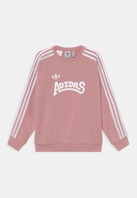 Rosa Adidas-tröja med vita tre ränder på ärmarna och vit Adidas-logotyp och text framtill, uppställd platt på vit bakgrund.
