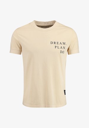 Camiseta de algodón beige con mangas cortas, cuello redondo y texto impreso "SUEÑA. PLANEA. HAZ." en la parte frontal en negro, con una etiqueta en el lateral.