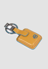 Gele lederen sleutelhanger met een blauwe accentrand, vierkante vorm en zilverkleurige metalen hardware. Voorzien van een lusbevestiging en een geperst logo.