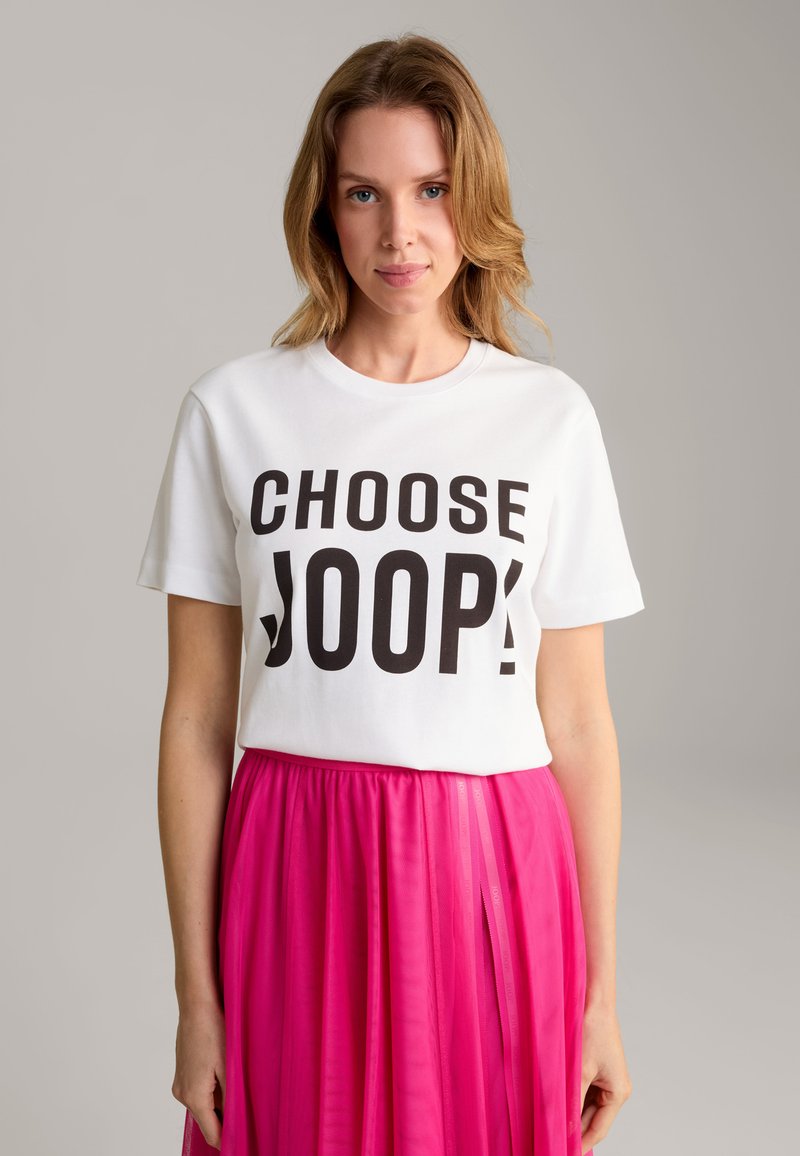 Witte katoenen t-shirt met vetgedrukt zwarte tekst "CHOOSE JOOP!" in combinatie met een vloeiende, geplisseerde roze rok. Zachte textuur, losse pasvorm.