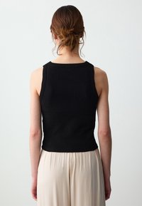 Top nero senza maniche realizzato in tessuto a coste, caratterizzato da una forma aderente e spalline larghe. Abbinato a pantaloni fluidi beige chiaro.