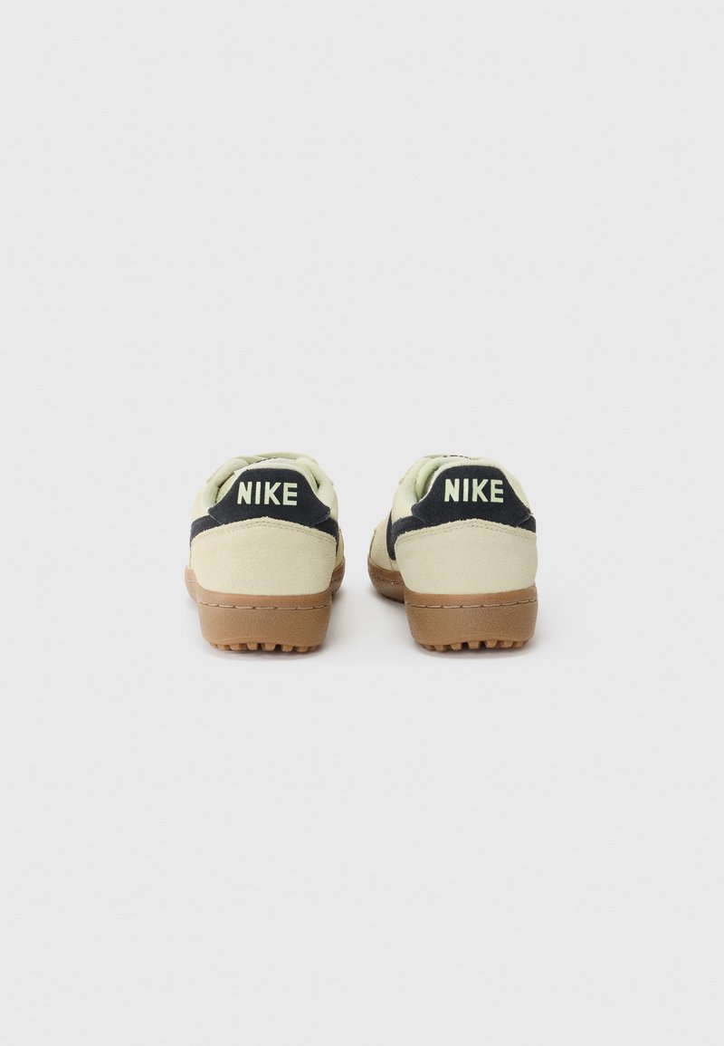 Baskets Nike avec un dessus en daim vert clair, des accents noirs et une semelle en caoutchouc marron. Présente une marque "NIKE" bien visible sur le talon.
