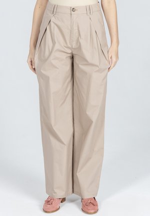 Beżowe spodnie z wysokim stanem i szerokimi nogawkami, z przednimi zakładkami, guzikiem z przodu i zamkiem błyskawicznym, w połączeniu z różowymi mokasynami z frędzlami na białym tle.