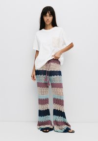Witte T-shirt met korte mouwen en een textuurzak, gecombineerd met multiculturele gestreepte gehaakte broek in tinten blauw, paars en room.