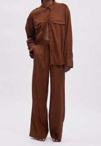 Ensemble marron deux pièces composé d'une chemise ample à boutons avec deux poches poitrine et d'un pantalon large assorti à taille élastique.