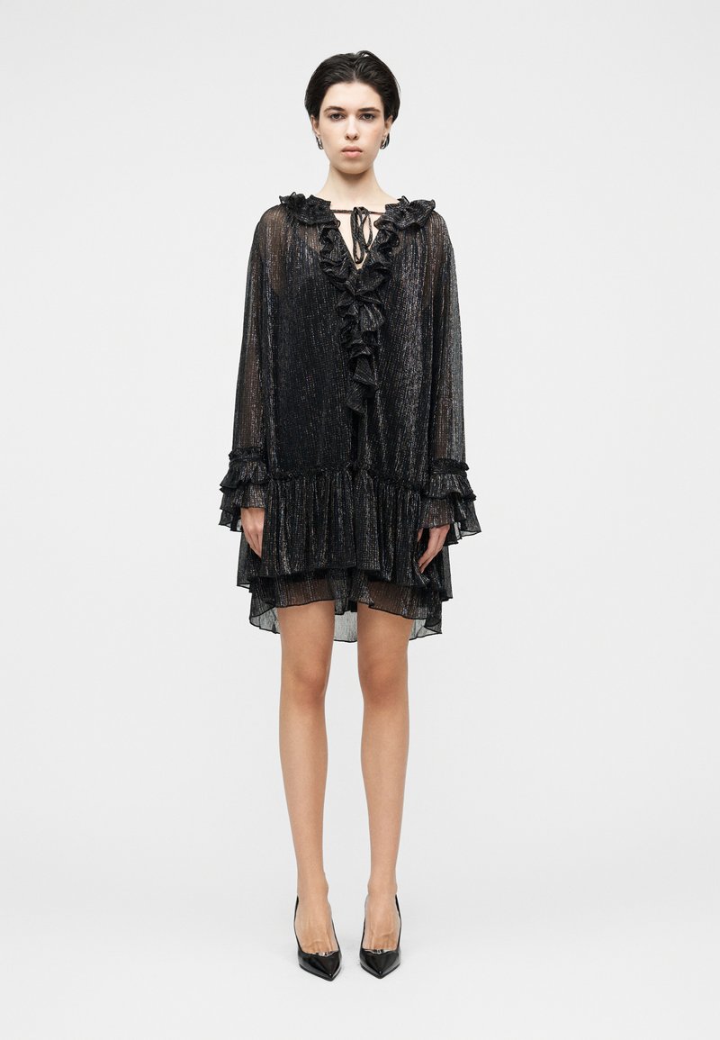 Μαύρο, διάφανο φόρεμα με λαιμόκοψη με βολάν και μ ακριά μανίκια. Διαθέτει στρώσεις και ασύμμετρο τελείωμα. Φορεμένο με μαύρες μυτερές γόβες.