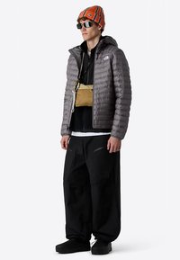 Gray puffer jacket with a fitted shape, black layered top, oversized black pants, and an orange striped beanie. Includes a small beige waist bag.