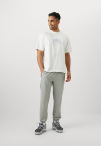 Hvid kortærmet t-shirt med blåt Nike-logo, parret med lysegrå sweatpants og grå sneakers med mørke accenter.
