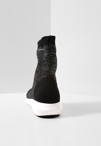Schwarze Knöchelsocken-Sneaker mit einem gestrickten Obermaterial, strukturierter Oberfläche und kontrastierender weißer Gummisohle; Logo in der Nähe der Oberseite sichtbar.