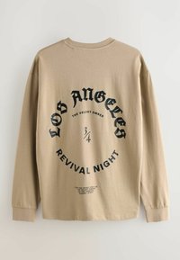 Langærmet beige t-shirt med et rundt sort grafisk design, der siger "LOS ANGELES REVIVAL NIGHT" med fed skrift; blød, bomulds tekstur.